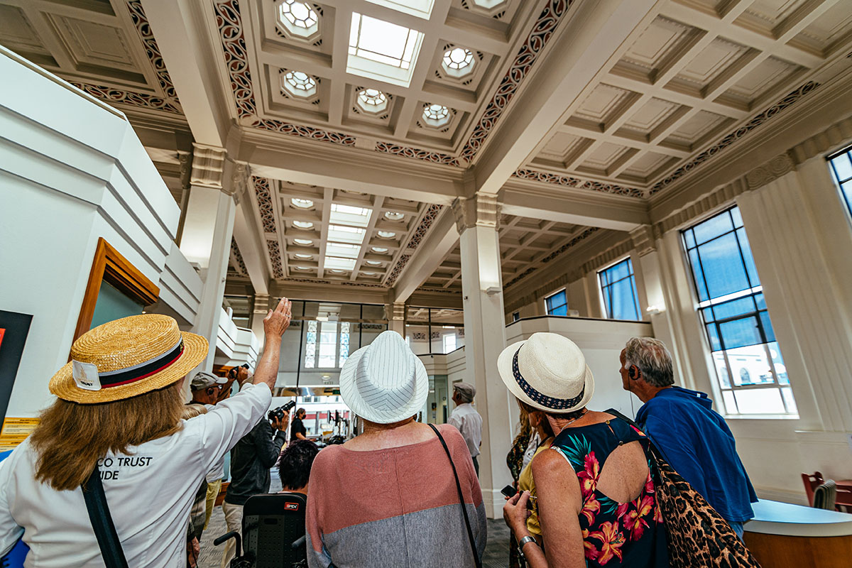 A group of tourist watch as a guide points to an architectural detail inside a building